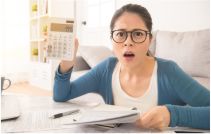 Shocked woman holding bills and calculator 